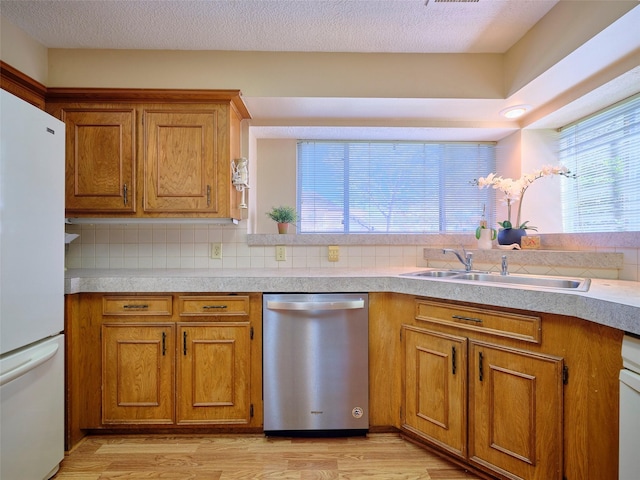 kitchen featuring brown cabinetry, light wood-style flooring, freestanding refrigerator, a sink, and stainless steel dishwasher