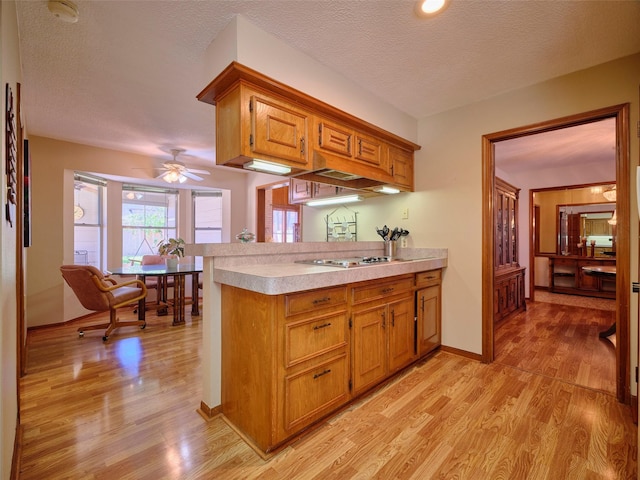 kitchen featuring light wood finished floors, stainless steel stovetop, brown cabinetry, and light countertops