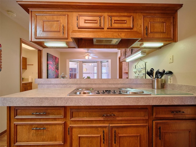 kitchen with electric cooktop, brown cabinets, light countertops, and ceiling fan