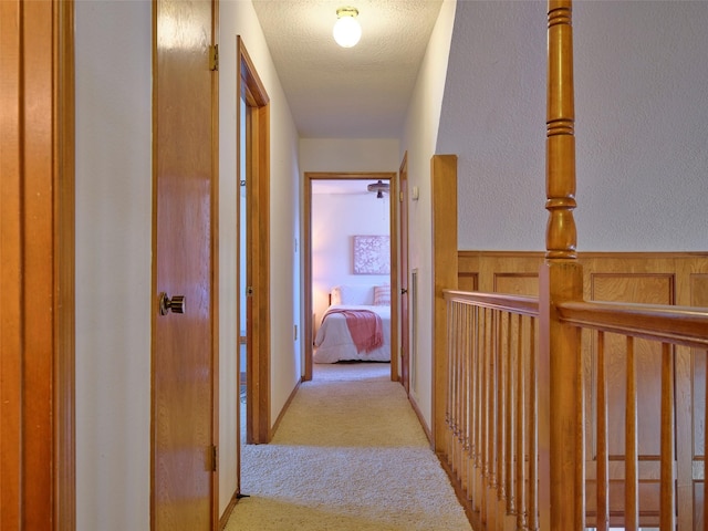 hall featuring a wainscoted wall, a textured ceiling, and carpet flooring