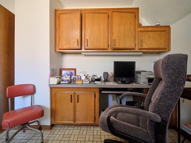 office area with a textured ceiling, brick floor, and built in study area