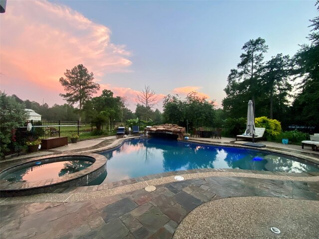 pool at dusk with a pool with connected hot tub, a patio area, and fence