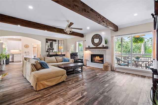 living room with arched walkways, a ceiling fan, wood finished floors, beamed ceiling, and a fireplace