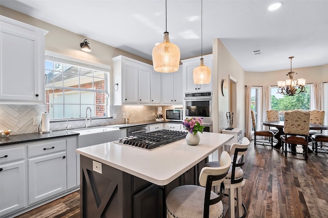 kitchen with dark wood-style flooring, white cabinets, appliances with stainless steel finishes, decorative backsplash, and a center island