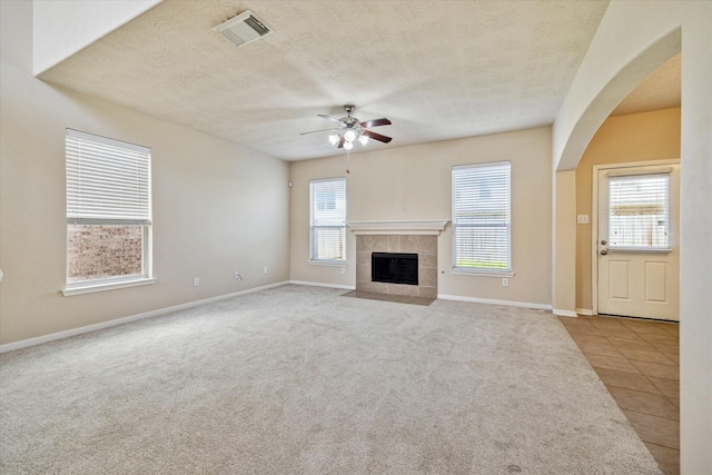 unfurnished living room with a fireplace, visible vents, carpet flooring, a textured ceiling, and tile patterned flooring