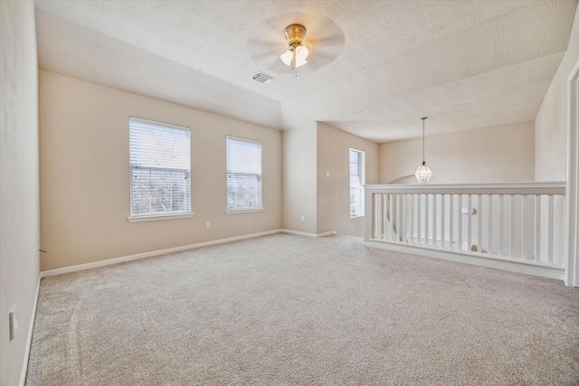 empty room featuring a textured ceiling, carpet floors, ceiling fan, and visible vents