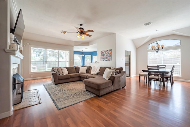 living room with ceiling fan with notable chandelier, a tile fireplace, visible vents, and wood finished floors