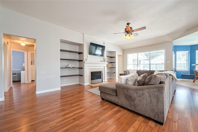 living room featuring attic access, baseboards, a ceiling fan, a glass covered fireplace, and wood finished floors