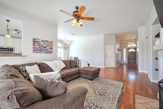 living area featuring ceiling fan with notable chandelier, vaulted ceiling, baseboards, and wood finished floors