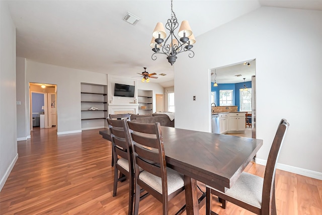 dining space with a fireplace, visible vents, wood finished floors, and ceiling fan with notable chandelier