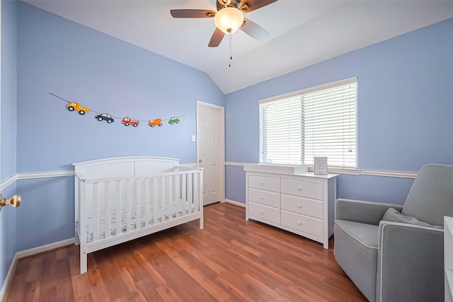 bedroom featuring baseboards, a ceiling fan, wood finished floors, vaulted ceiling, and a nursery area