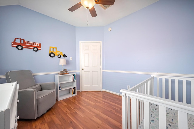 bedroom with ceiling fan, lofted ceiling, wood finished floors, baseboards, and a crib