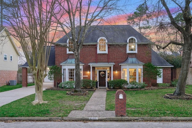 view of front facade with central AC, brick siding, fence, driveway, and a front yard