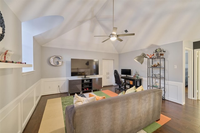 living room with a wainscoted wall, dark wood finished floors, a decorative wall, a ceiling fan, and vaulted ceiling