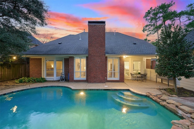 rear view of property with a fenced in pool, a patio area, fence, and roof with shingles