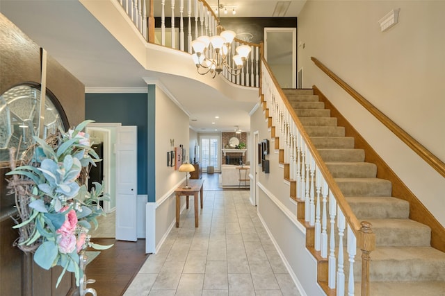 foyer entrance featuring stairway, a high ceiling, crown molding, a brick fireplace, and a notable chandelier