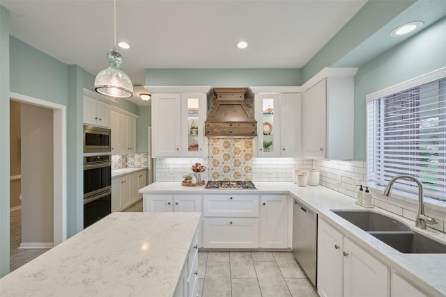 kitchen with appliances with stainless steel finishes, light stone countertops, custom exhaust hood, white cabinetry, and a sink