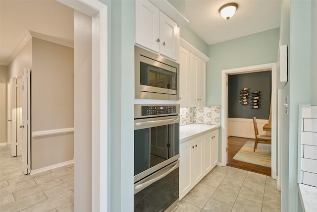 kitchen with appliances with stainless steel finishes, light countertops, crown molding, white cabinetry, and backsplash