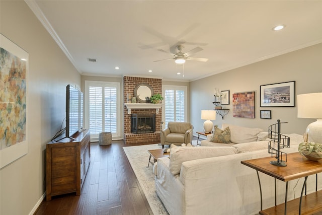 living room with dark wood-style flooring, a fireplace, visible vents, a ceiling fan, and ornamental molding