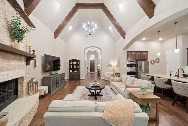 living room with high vaulted ceiling, arched walkways, a stone fireplace, dark wood-type flooring, and a notable chandelier