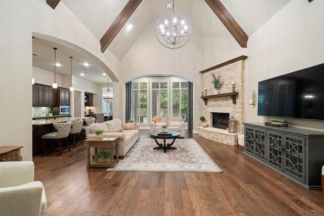 living room featuring a stone fireplace, an inviting chandelier, arched walkways, high vaulted ceiling, and dark wood-style flooring