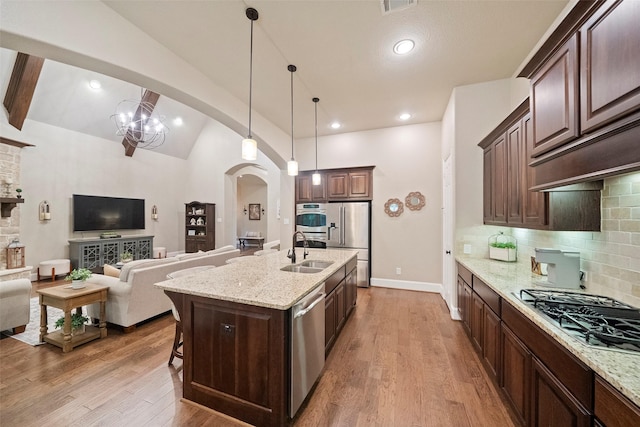 kitchen featuring a sink, stainless steel appliances, arched walkways, and wood finished floors