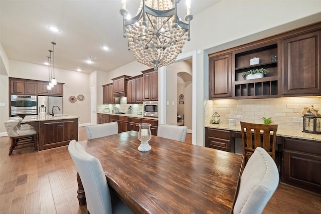 dining space featuring wood finished floors, recessed lighting, arched walkways, an inviting chandelier, and baseboards