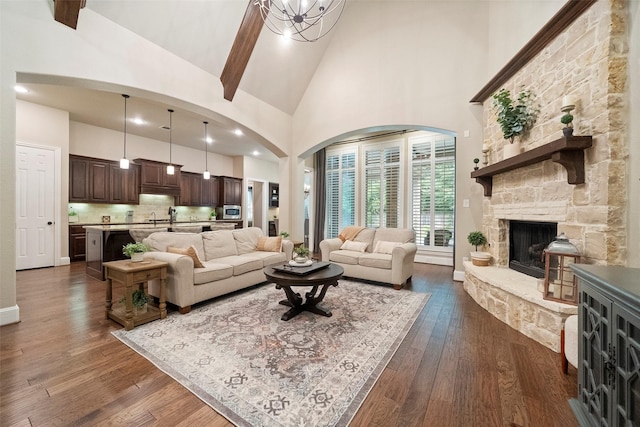 living room with high vaulted ceiling, dark wood finished floors, beam ceiling, an inviting chandelier, and a fireplace