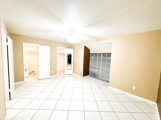 spare room with washer / dryer, light tile patterned floors, baseboards, ceiling fan, and a textured ceiling