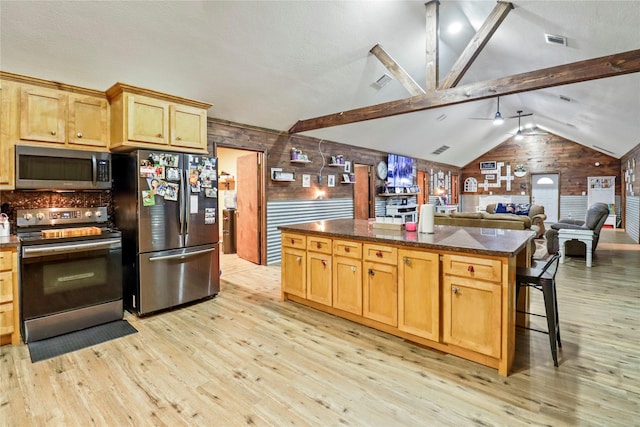 kitchen with vaulted ceiling with beams, appliances with stainless steel finishes, a kitchen island, light wood-type flooring, and a kitchen breakfast bar