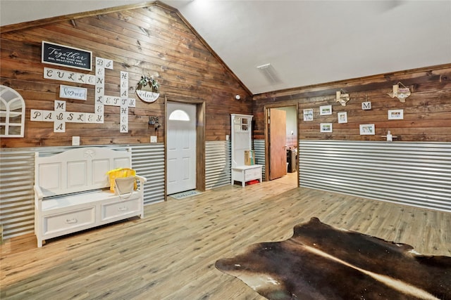 living area with light wood-style floors, lofted ceiling, and wooden walls