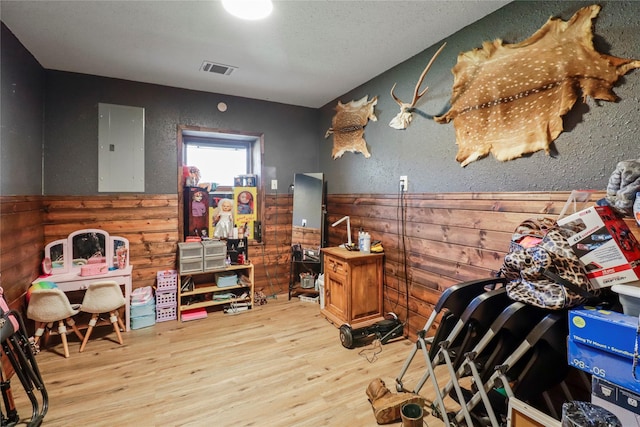 miscellaneous room featuring a textured wall, wood finished floors, visible vents, wainscoting, and electric panel