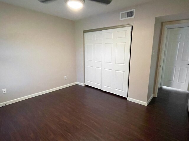 unfurnished bedroom featuring dark wood-type flooring, a ceiling fan, visible vents, baseboards, and a closet