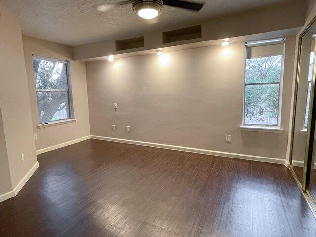 empty room with a textured ceiling, ceiling fan, dark wood-type flooring, and baseboards