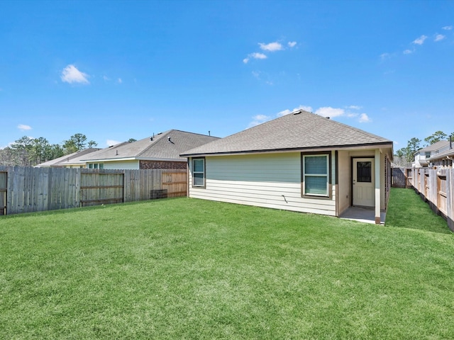 rear view of property featuring a fenced backyard, a shingled roof, and a yard