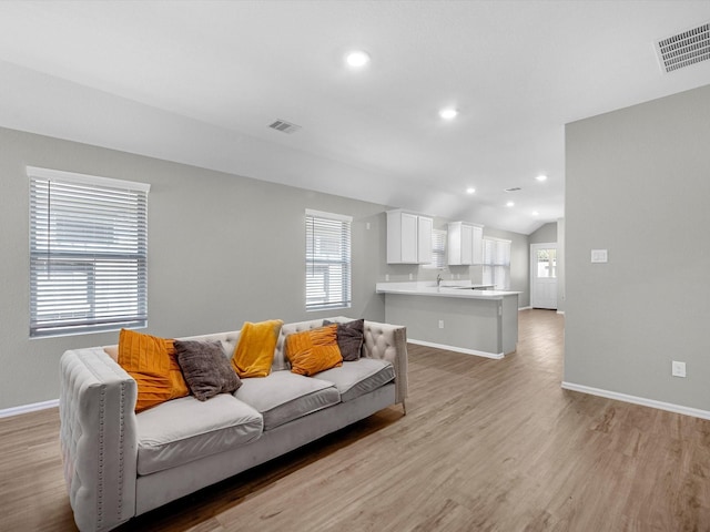 living room featuring vaulted ceiling, baseboards, visible vents, and light wood-type flooring