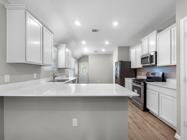 kitchen with visible vents, appliances with stainless steel finishes, a peninsula, light wood-style floors, and a sink