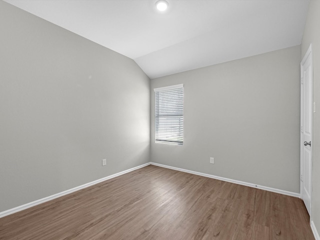 empty room featuring lofted ceiling, wood finished floors, and baseboards