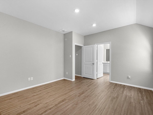 unfurnished bedroom with wood finished floors, baseboards, ensuite bath, lofted ceiling, and recessed lighting