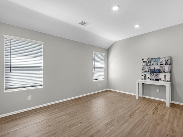 empty room featuring lofted ceiling, light wood-style flooring, baseboards, and visible vents