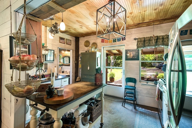 kitchen with unfinished concrete flooring, wooden ceiling, freestanding refrigerator, and wooden walls