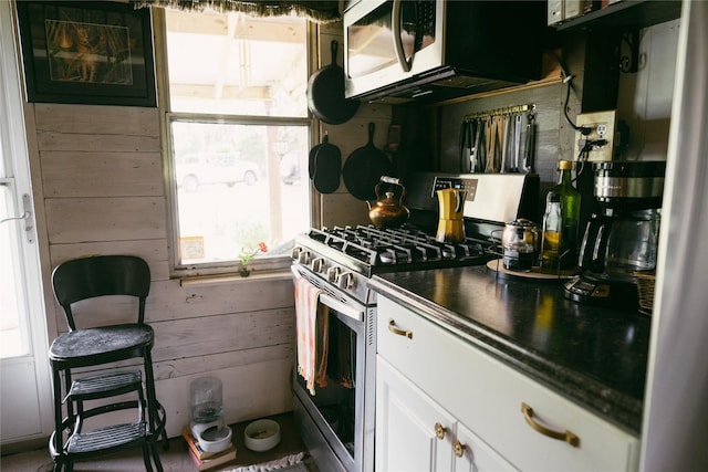 kitchen with dark countertops, white cabinetry, wooden walls, and gas range