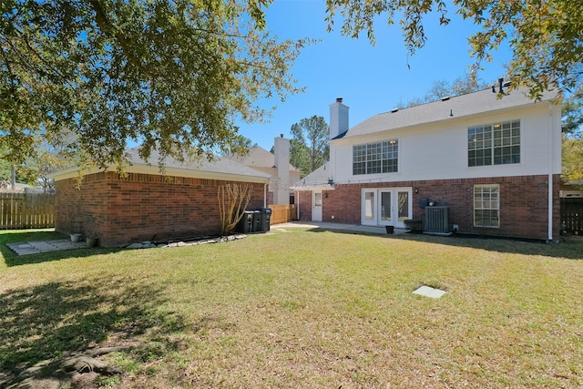 back of house featuring french doors, brick siding, central AC unit, and a yard