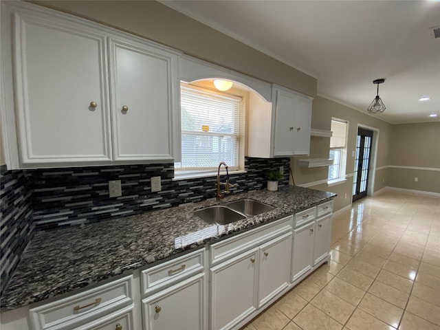 kitchen featuring light tile patterned floors, a wealth of natural light, white cabinets, a sink, and backsplash