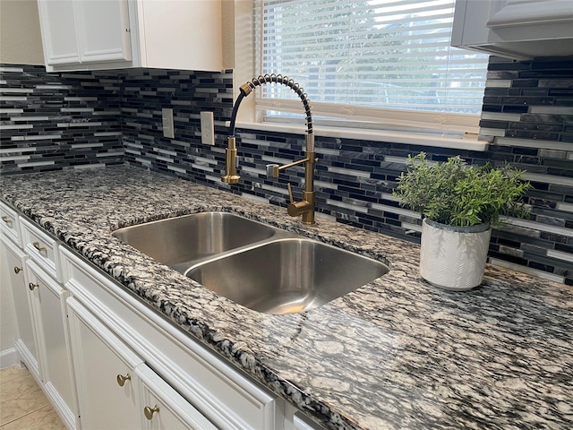 room details with backsplash, dark stone countertops, white cabinets, and a sink