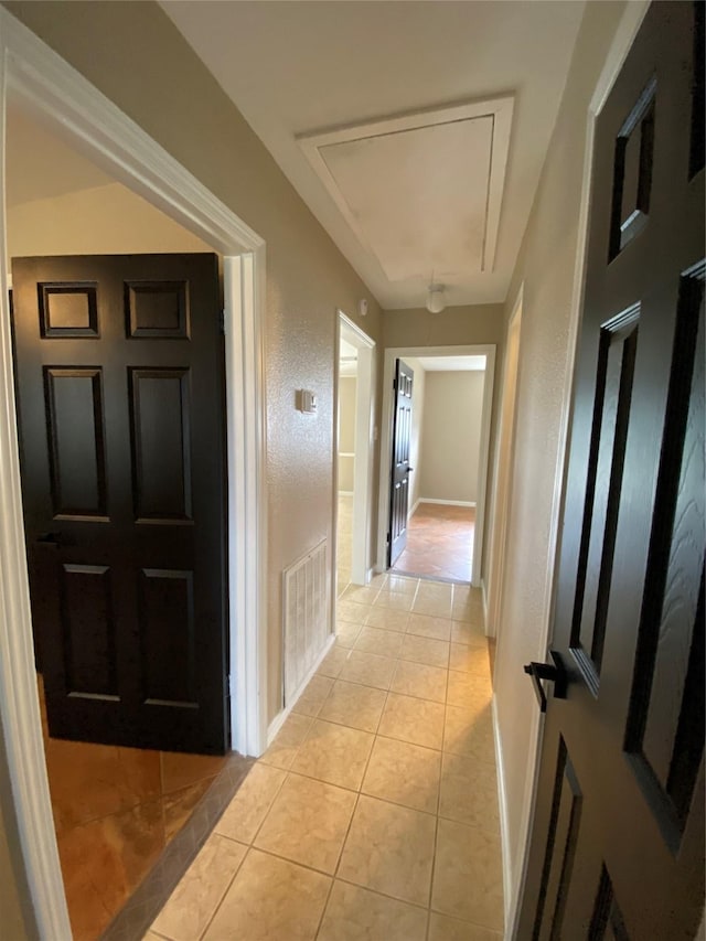 corridor featuring light tile patterned floors, attic access, visible vents, and baseboards