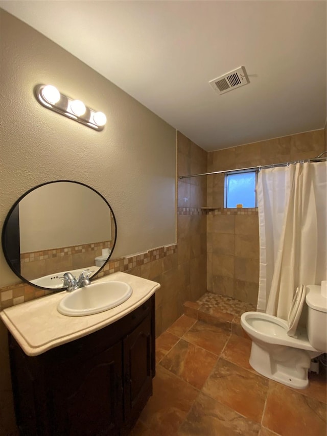 bathroom with toilet, vanity, visible vents, tile walls, and a tile shower