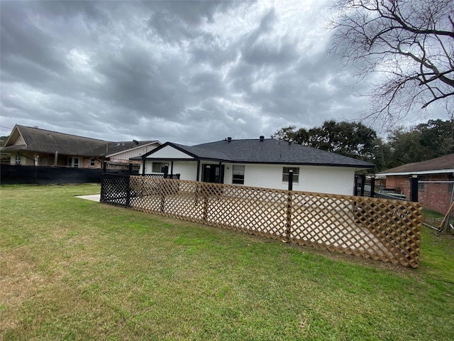 back of house featuring a shingled roof, fence, and a lawn