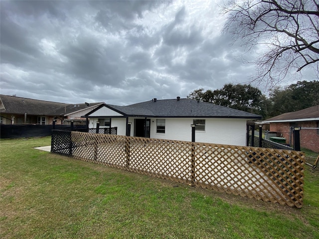 rear view of property featuring roof with shingles, fence, a lawn, and brick siding