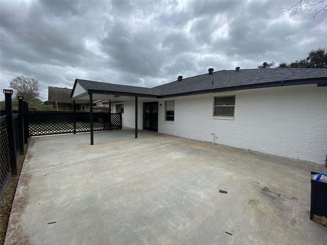 rear view of house with a patio, brick siding, roof with shingles, and fence